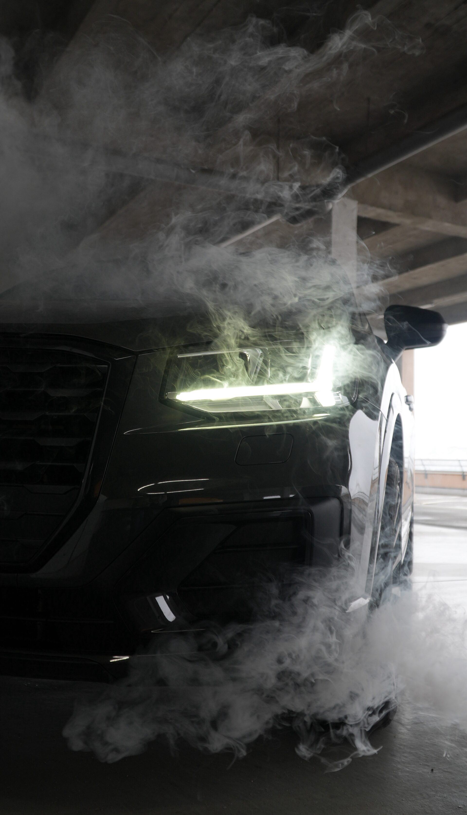 Audi phares allumés dans un nuage de fumée, sous un parking couvert