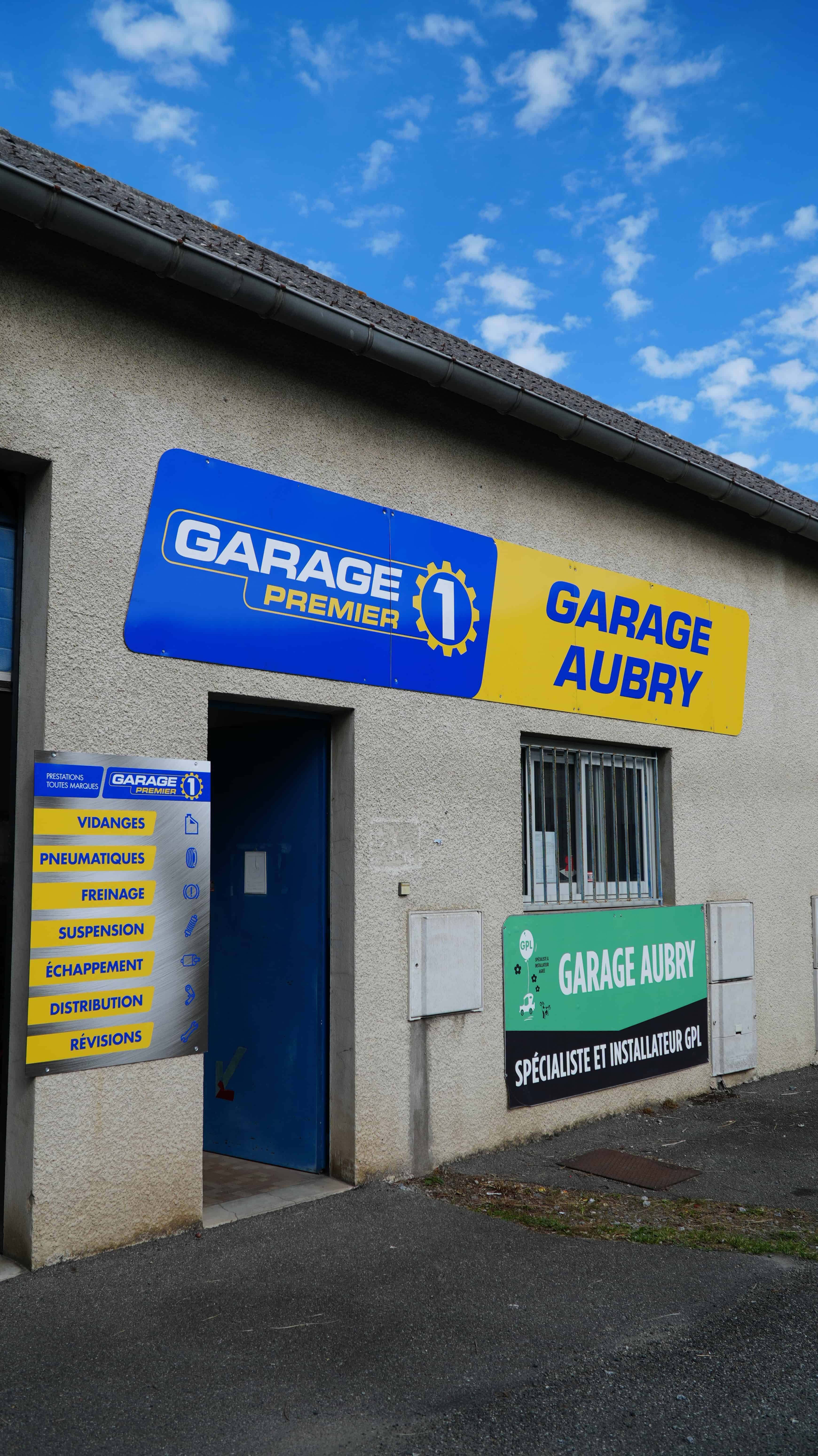 Façade du Garage Aubry sous un ciel bleu, enseignes bleue et jaune