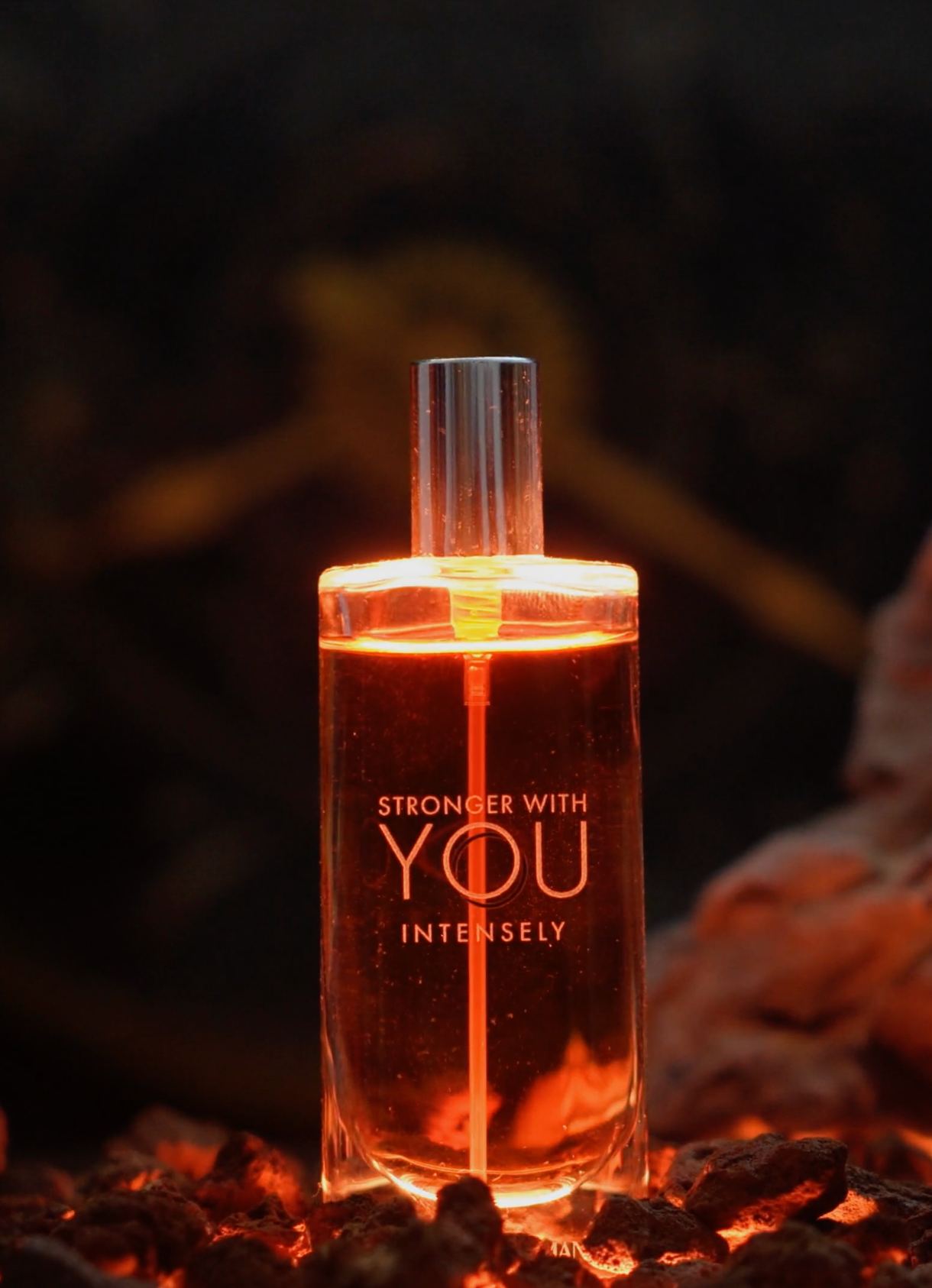 Flacon de parfum Stronger With You éclairé de l’intérieur, posé sur des braises