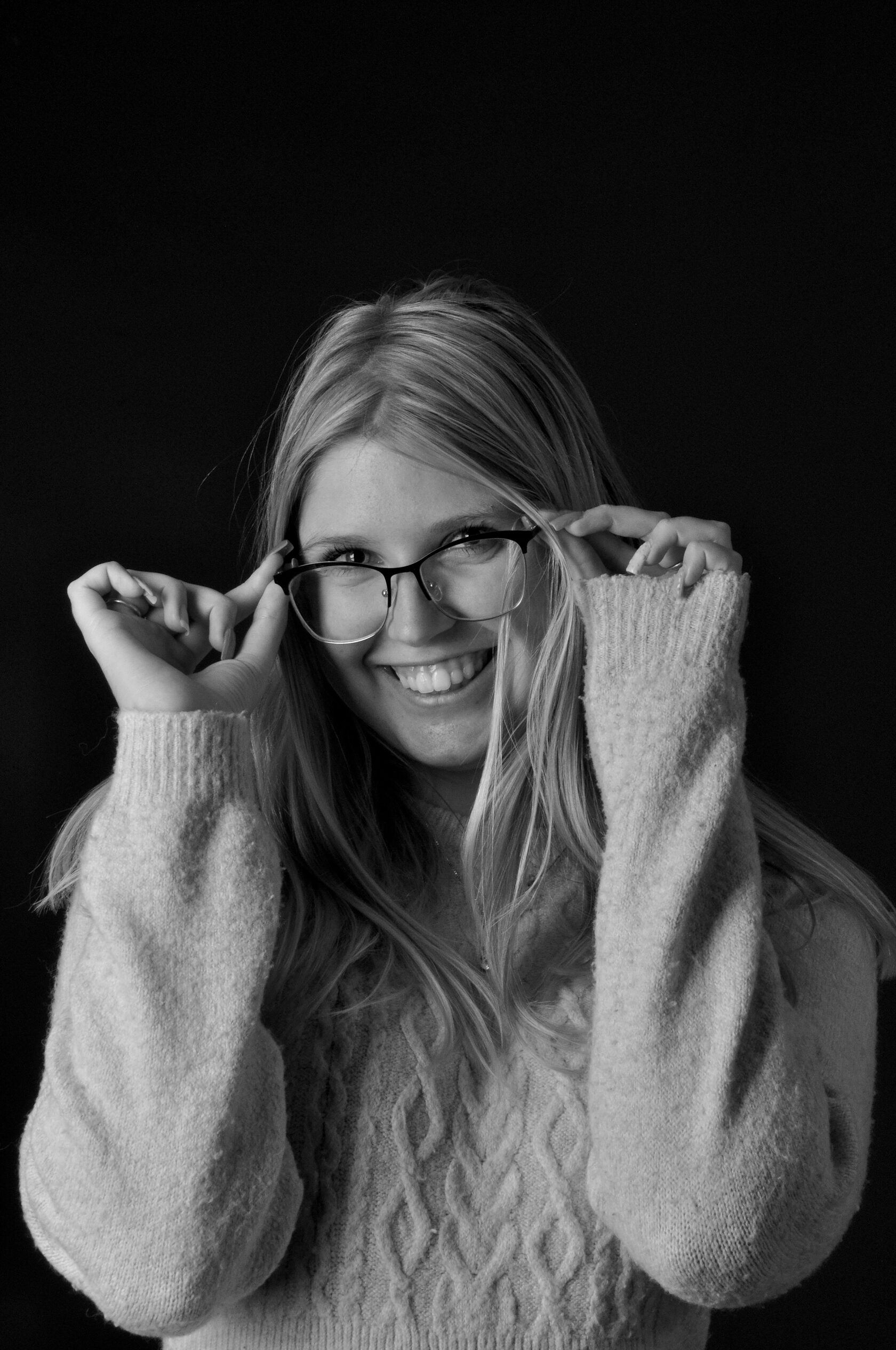 Portrait en noir et blanc d’une femme souriante ajustant ses lunettes