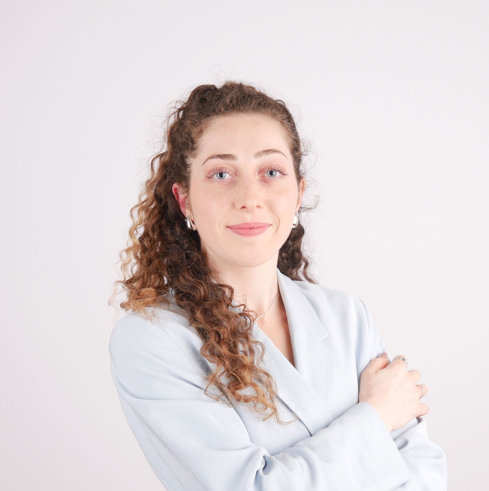 Portrait d’une femme aux cheveux bouclés sur fond clair, bras croisés