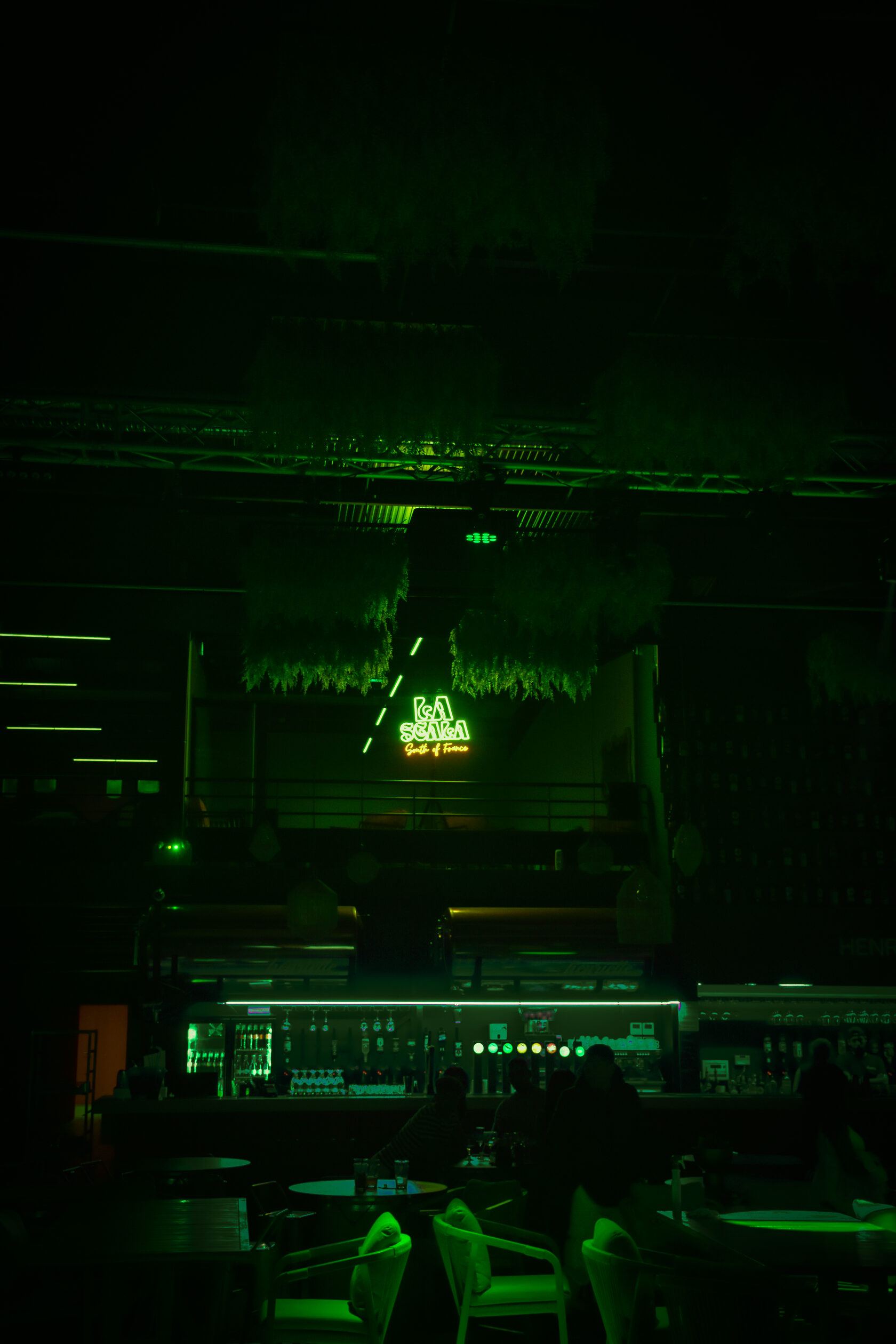 Salle de La Scala baignée de lumière verte, enseigne néon au-dessus du bar